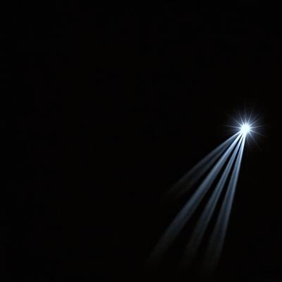 The primary subject of the image is a bright light source, possibly a star or a light bulb, shining in the darkness. The setting is a black background, which contrasts with the bright light source. The visual style appears to be a photo, as the light source is captured in a dark environment. The colors and mood of the image are predominantly dark, with the bright light source being the main focal point.